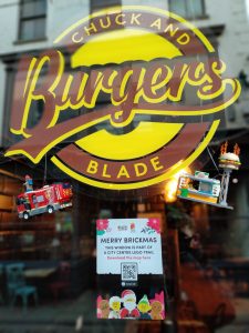 A photo of Chuck and Blade Burgers with a merry brickmas - this window is a part of a city centre Lego trail - sign below it