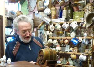 A photo of an older man in a shop, with displays of mugs, glassware and crockery in the background